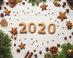Gingerbread of the form of numbers 2020 new year ginger cookies, confetti gold stars, spices and firs on white wood background. Top view.