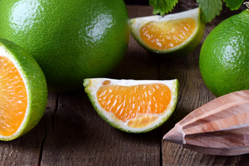 Green mandarins cut in halves and segments and whole sweetie on a wooden table