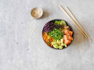 Hawaiian salmon poke bowl with rice, avocado, cucumber, carrot, red cabbage, chukka and sesame seeds on a gray background. top view