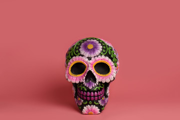The black skull is decorated with purple and pink flowers. Da de los Muertos  Halloween project. The skull is isolated on a pink background and is located in the center.