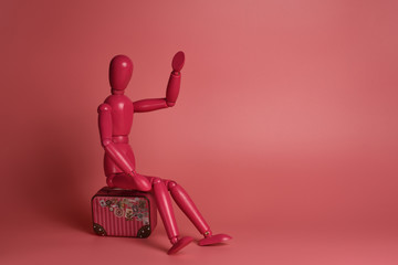 A pink wooden man sits on a suitcase against a pink background. Isolated. Business, selling out, late, waiting, flying concept. Copy space, banner, postcard.