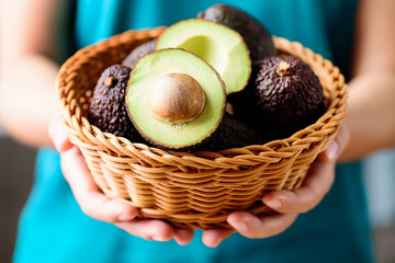 Woman hand holding basket of ripe hass avocado fruit