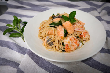 Stir-fried spaghetti with salmon, shrimp and stomach in a white bowl on a wooden table