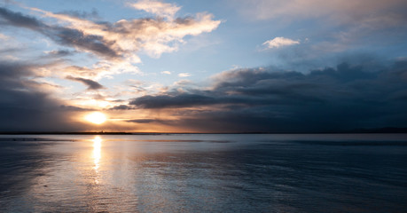 Fototapeta na wymiar Stunningly beautiful sunrise, taken on a cloudy morning from Salthill beach near Galway, Ireland. Showing the calm water of Galway Bay and Mutton Island in the distance.