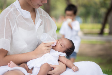 Beautiful Asian young mother  or single mom with new born baby girl are feeding milk from bottle in the park. concept of duties of wife and mother in raising children.