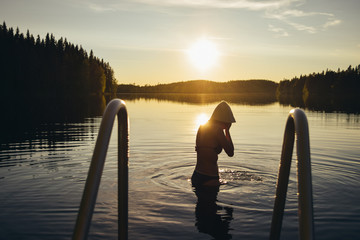 Young woman swimming in the lake at sunset after sauna in Finland