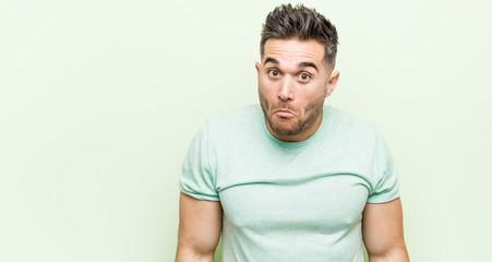 Young handsome man against a green background shrugs shoulders and open eyes confused.