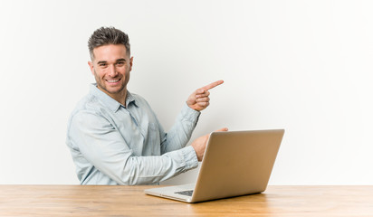 Young handsome man working with his laptop excited pointing with forefingers away.