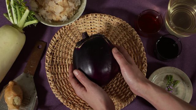 a Japanese female chef picking up KAMONASU (Japanese round aubergine) from her kitchen table, Tokyo, Japan. July 2019. Camera fixed, close up, bird's eye view