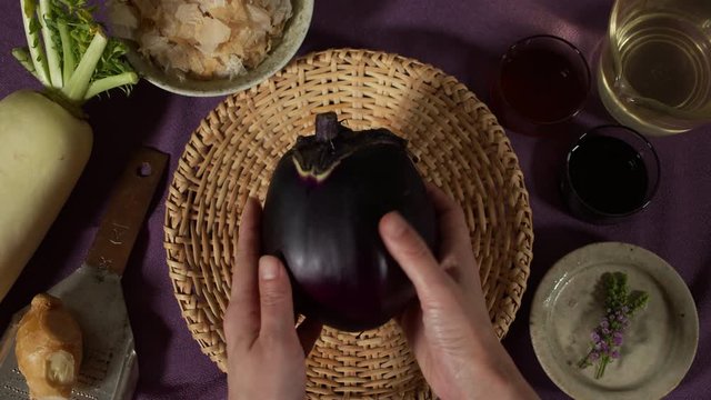 a Japanese female chef checks and puts KAMONASU (Japanese round aubergine) on kitchen table, Tokyo, Japan. July 2019. Camera fixed, close up, bird's eye view