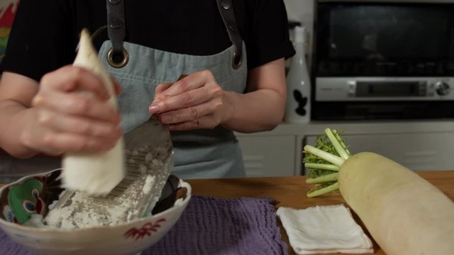 a Japanese female chef grating DAIKON (Mooli) at her home kitchen, Tokyo, Japan. July 2019. Camera fixed, close up, high view,