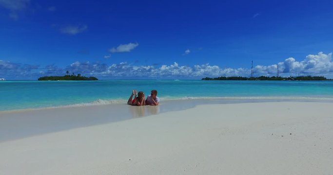 Guy and girl sunbathing on shallow warm water on beach with bright colorful background of tiny tropical islands in Caribbean