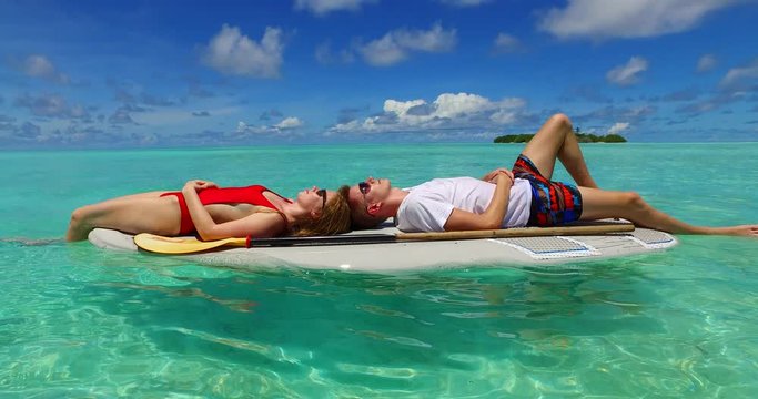 Zooming to couple sunbathing over swimming board oscillated from sea waves in Mentawai Islands, Indonesia