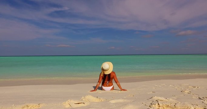 Lonely young woman with white hat watching horizon line of turquoise water and cloudy sky, relaxing on empty beach of Banton island
