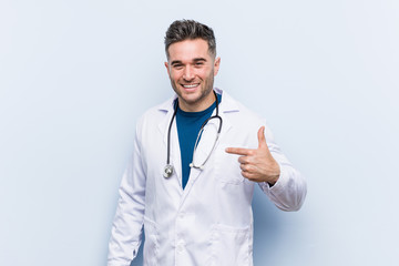 Young handsome doctor man person pointing by hand to a shirt copy space, proud and confident