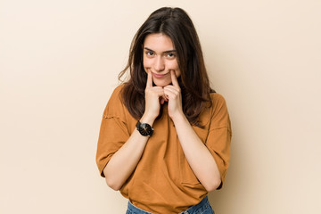 Young brunette woman against a beige background doubting between two options.