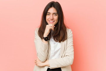 Young brunette business woman against a pink background smiling happy and confident, touching chin with hand.