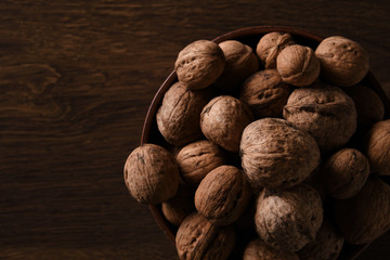  Walnuts nuts in a bowl on a dark brown wooden background in a dark key