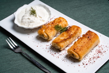 Fried pancakes with sour cream on a white plate.