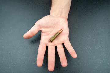A green 7.62 mm cartridge for a Kalashnikov assault rifle lying in a man's hand against a green...