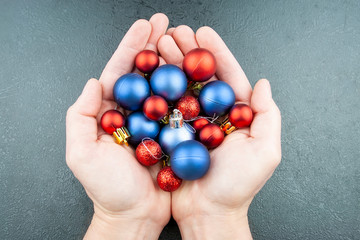 Hands filled with small blue and red Christmas balls against a gray background