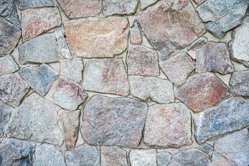 A wall of large rough uneven granite stones with cement grout between them