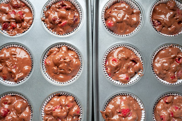 Top view of paper muffin molds with corrugated sides, filled with chocolate dough with cherries in teflon baking dish. Preparation before baking cupcakes before loading into the oven