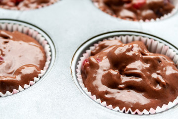 Closeup view of paper muffin molds with corrugated sides, filled with chocolate dough with cherries in teflon baking dish. Preparation before baking cupcakes before loading into the oven