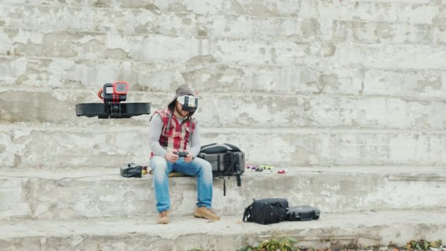 A man in a helmet with telemetry controls a drone that flies in front of him