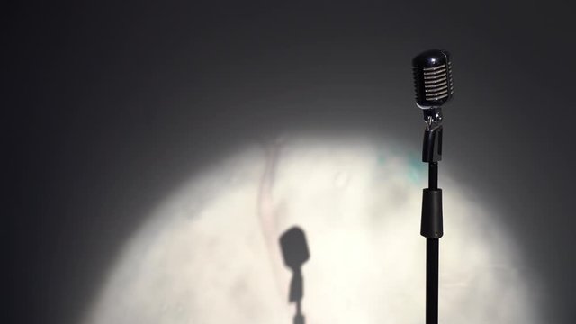 Professional classic vintage glare microphone for record or speak to audience on stage in dark empty retro club close up. Round spotlights shine on a chrome mic on the right on gray background.