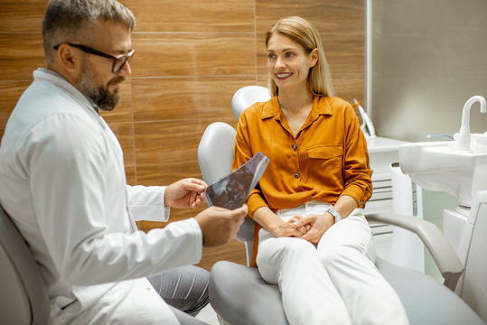 Beautiful woman as a patient with senior dentist during a medical consultation at the dental office, doctor showing x-ray image of a jaw