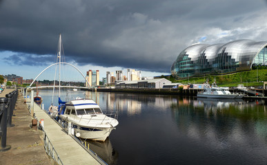 Fototapeta premium A yacht moored at Newcastle's Quayside with the Baltic Art Museum, Gateshead Sage and Millennium Bridge in the distance.