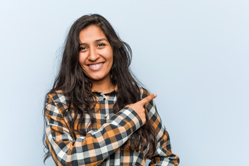 Fototapeta premium Young cool indian woman smiling and pointing aside, showing something at blank space.