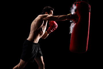 Strong man punching a bag on a black background