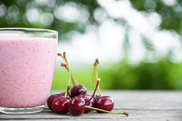 A glass of fresh cold smoothie with berries and cherrys on a wooden table, summer set, outdoor greed blured background,boke.