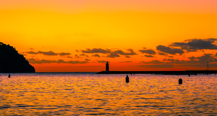 a lighthouse with an amazing sunset in the background with the orange sky reflecting in the water  