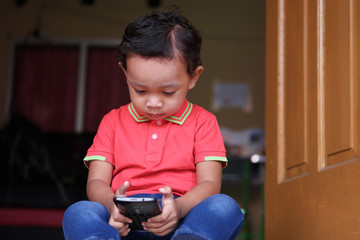 Little Asian boy uses smartphone at home