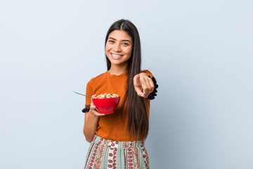 Young arab woman holding a cereal bowl cheerful smiles pointing to front.