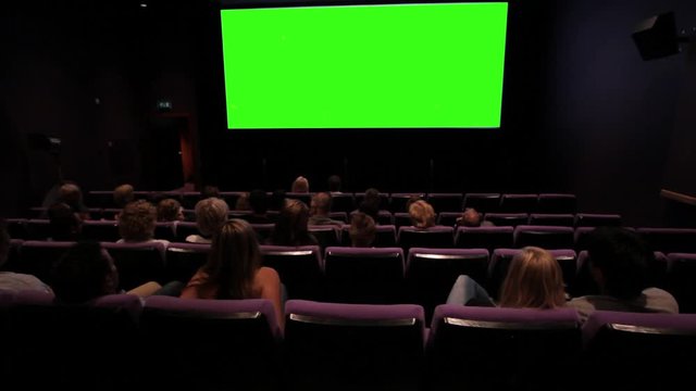 People in cinema, moviegoers sitting in cinema and watching big movie screen. Greenscreen. People shot from behind.