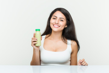 Young hispanic woman holding a vegetable drink happy, smiling and cheerful.