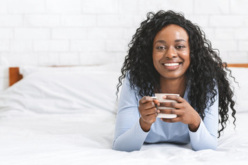 Happy girl relaxing in bed with cup of coffee