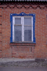 Antique wooden white window with blue carved frame and red brick wall without modern elements in the afternoon