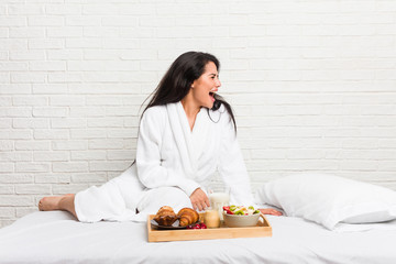 Young curvy woman taking a breakfast on the bed shouting towards a copy space