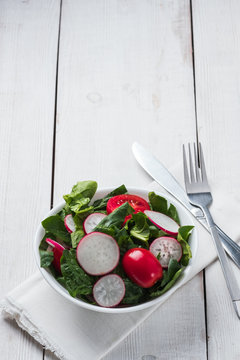 Fresh spring salad with green leaves of arugula, , spinach, beets, radish, cucumber and tomato on a gray stone background.