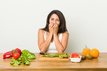 Young curvy woman preparing a healthy meal laughing about something, covering mouth with hands.