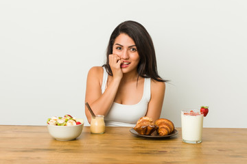 Obraz na płótnie Canvas Young curvy woman taking a breakfast biting fingernails, nervous and very anxious.