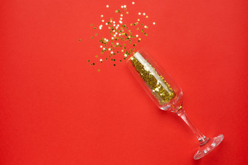 Champagne glass with golden stars confetti on red color paper background minimal style