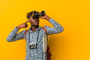 Young african tourist man standing against a yellow background holding a binoculars