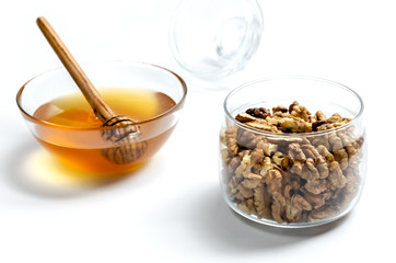 Jar with walnuts, a transparent saucer with honey and a spoon for honey, on a white isolated background. Tasty and healthy food.