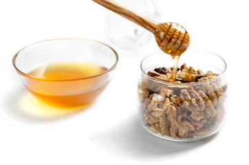 Jar with walnuts, a transparent saucer with honey on a white isolated background. Honey from a spoon flows into a jar of nuts. Close-up.